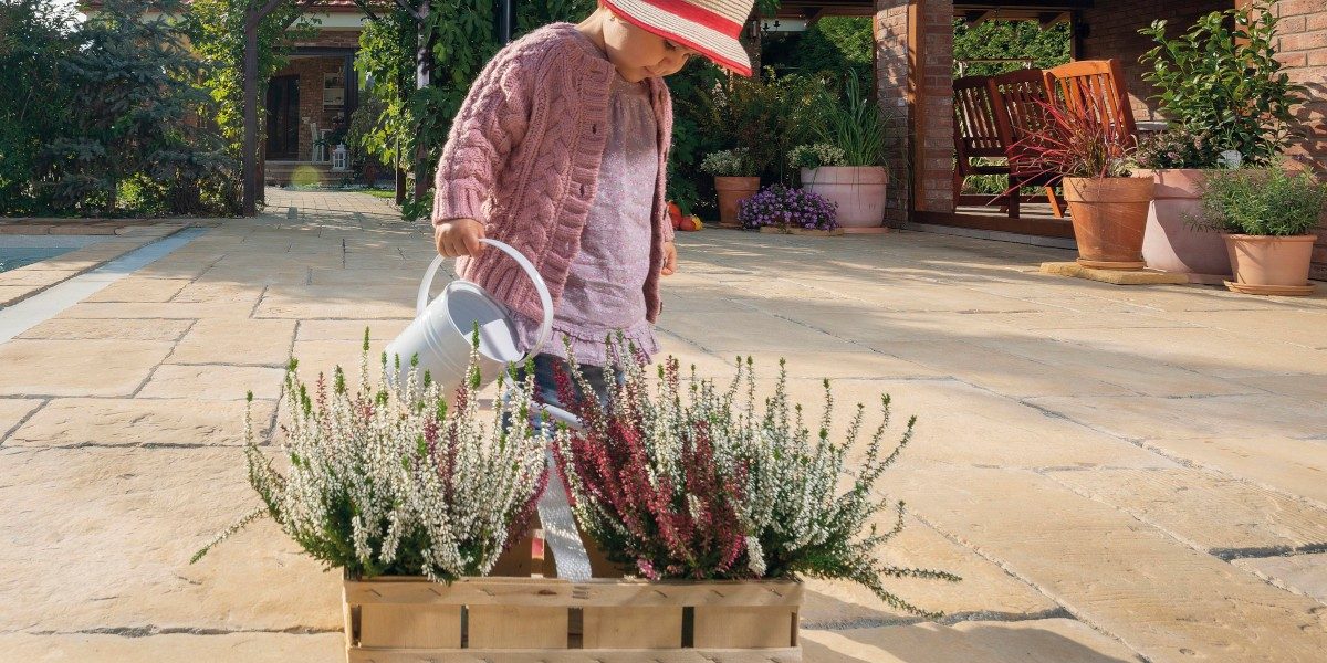 Djvojčica zalijeva cvijeće na terasi sa svijetlim opločnicima