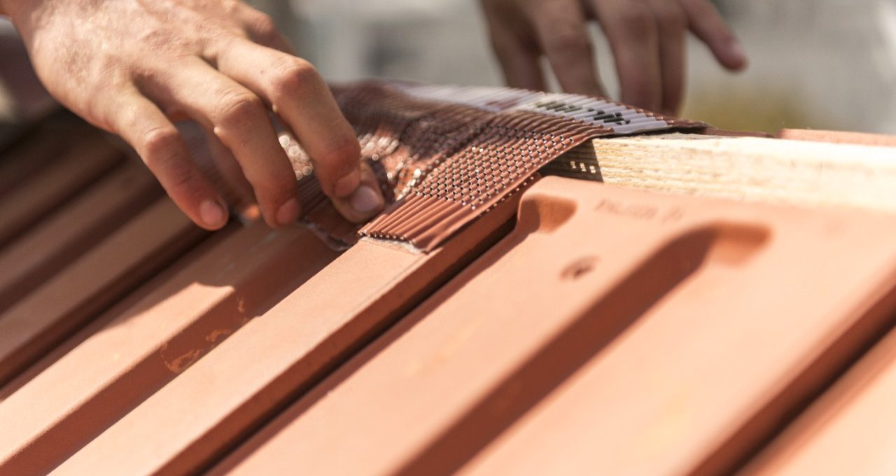 Roofer applying Alu-Grip Rol ridge and hip roll on ridge with bare hands