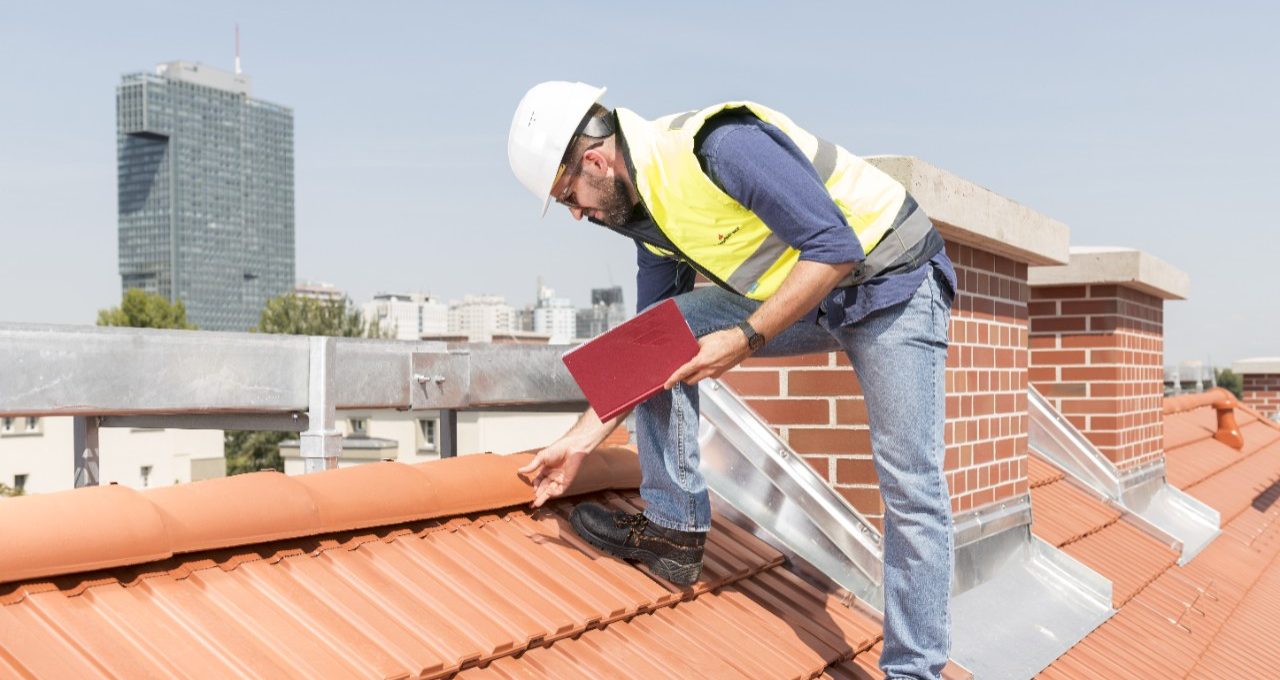 Urban roofers builder standing on roof checking toof tiles wearing hard hat and safety jacket