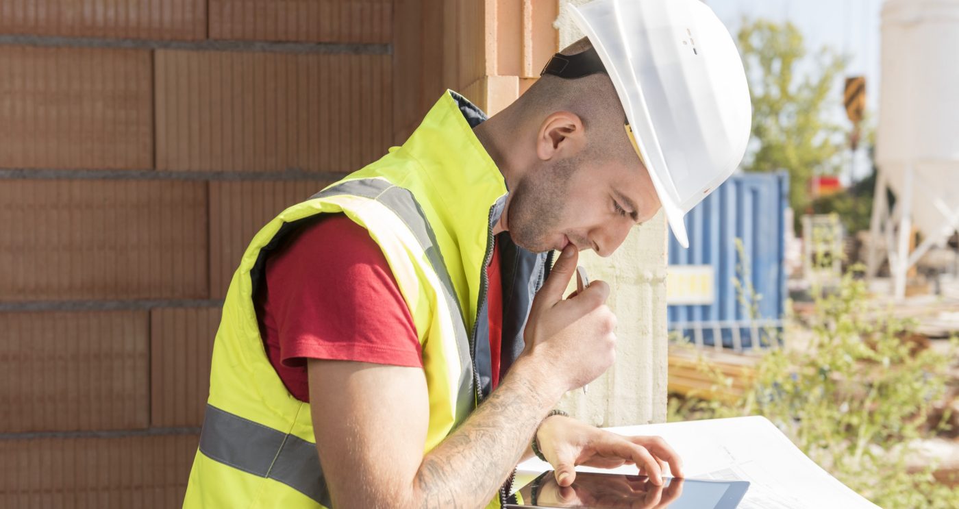 Construction worker working with tablet placed on blueprint in building shell