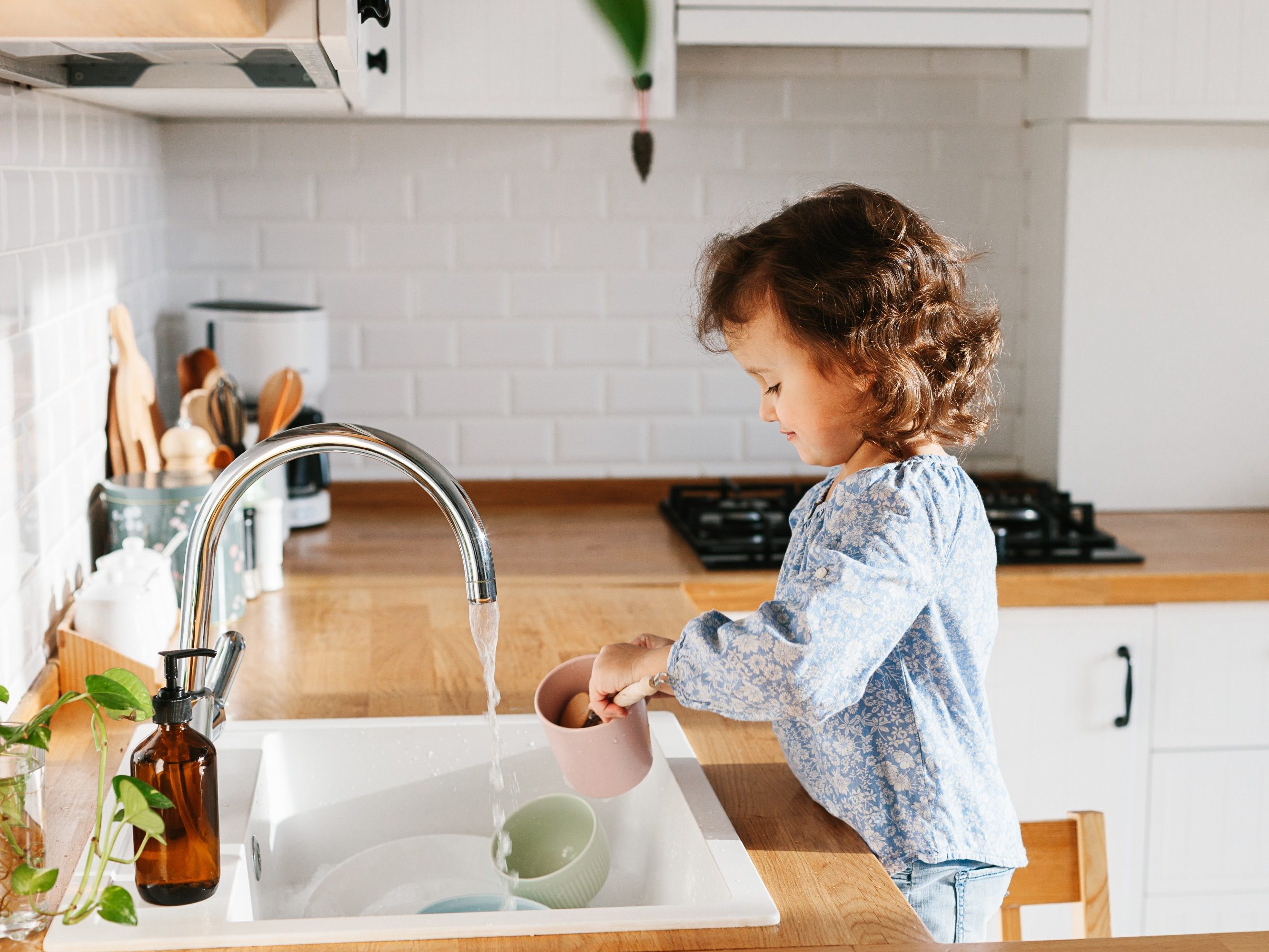 Djevojčica pod mlazom vode pere ruke u kuhinji
