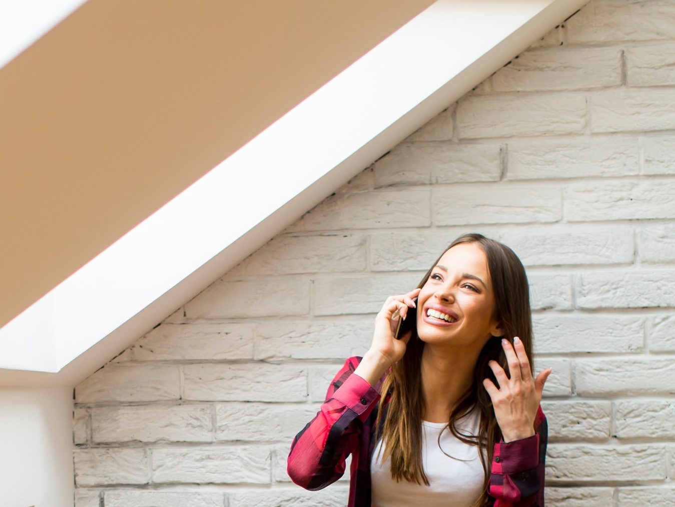 Djevojka stoji ispod krovnog prozora i razgovara na mobitel